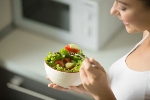 Bowl of fresh green salad hold in female hands, close up. Weight loss concept