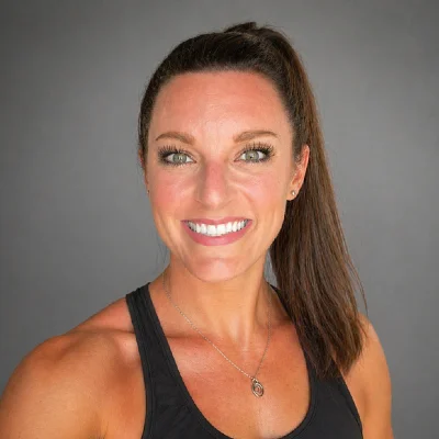 Smiling woman with brown hair in a high ponytail wearing a black tank top, against a gray backdrop.