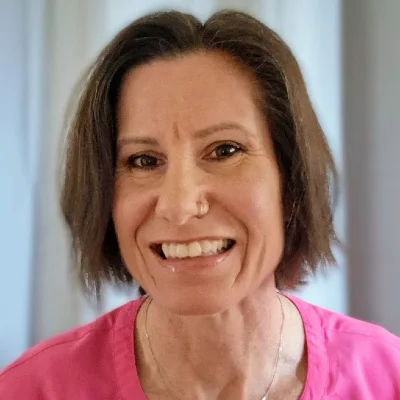 Portrait of a smiling woman with short brown hair wearing a pink top, neutral background behind her.