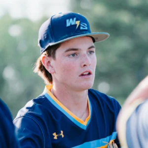 Young male athlete wearing a blue jersey with yellow trim and a matching blue cap, outdoors.