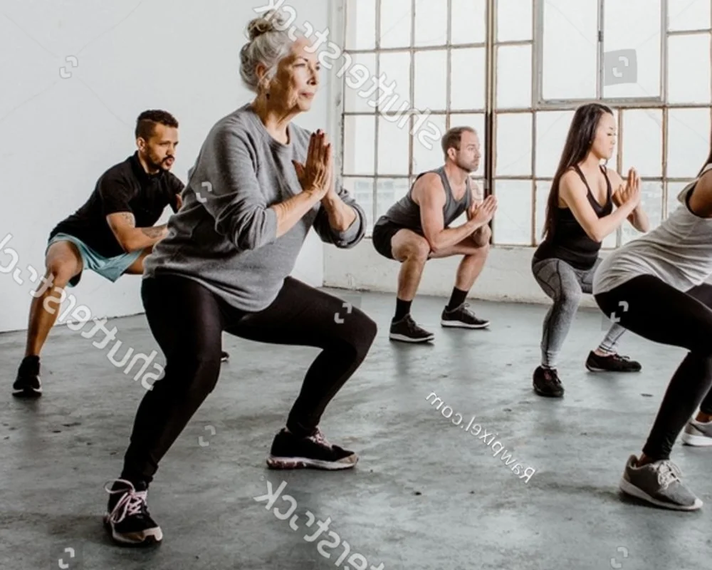 Group of adults in a bright studio performing squats with hands in prayer pose during a workout class.