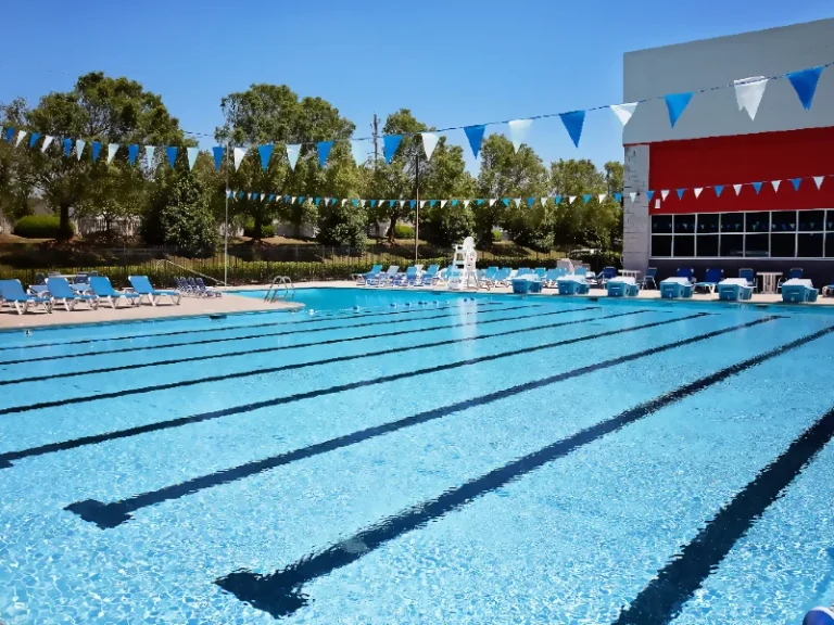 Outdoor swimming pool with lane lines, blue water, and rows of lounge chairs under pennant banners.
