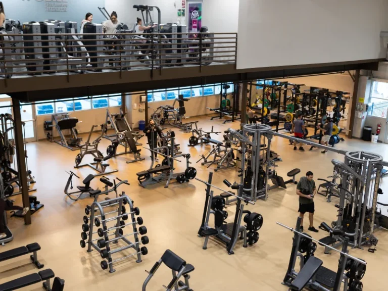 Spacious gym with weight machines and benches on the ground floor and cardio equipment on a balcony above.