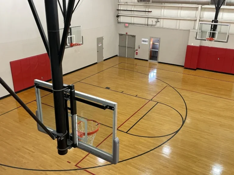 Basketball court seen from above with hoop and backboard in foreground and padded red walls on the sides