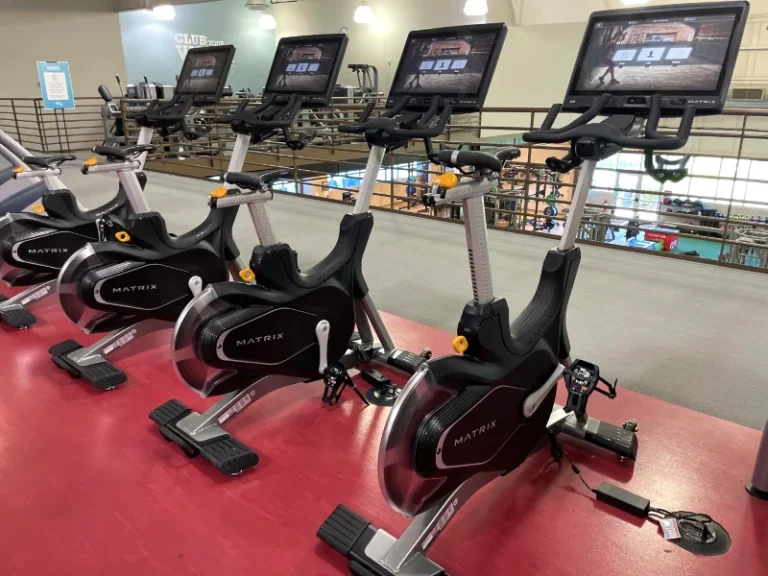 Row of Matrix indoor cycling bikes with large screens mounted above in a gym studio.